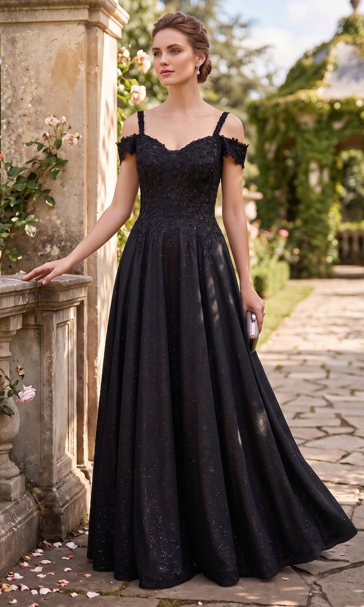 A woman stands outdoors on a stone path, surrounded by greenery and flowers, wearing the Long Prom Dress: Chicas J169 in black, featuring an embellished bodice and a glittering A-line skirt, and holding a small clutch.